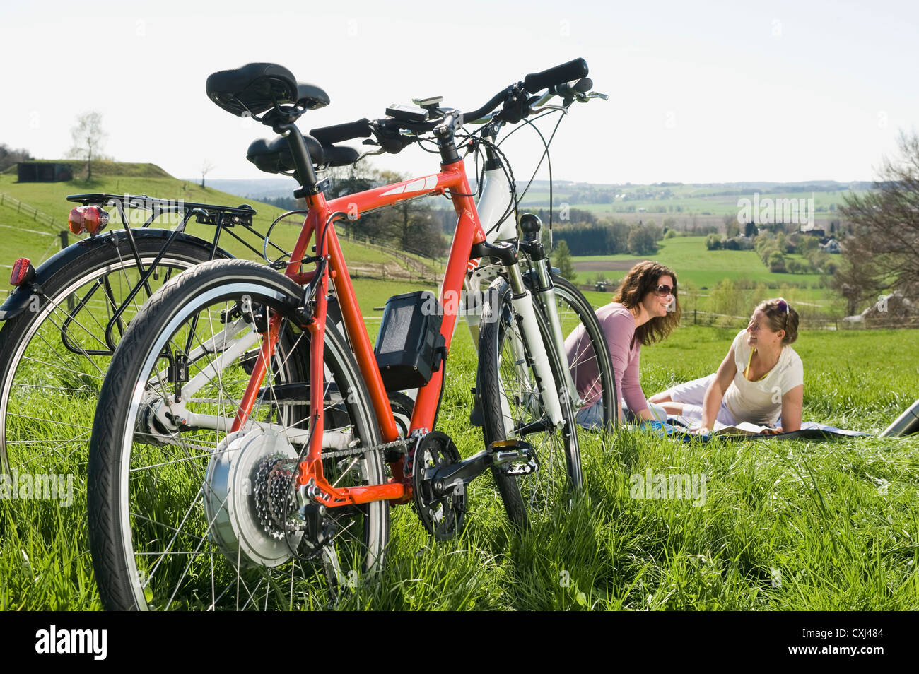 Deutschland, Bayern, Reife Frauen sitzen auf dem Rasen, Elektro-Fahrrad im Vordergrund Stockfoto