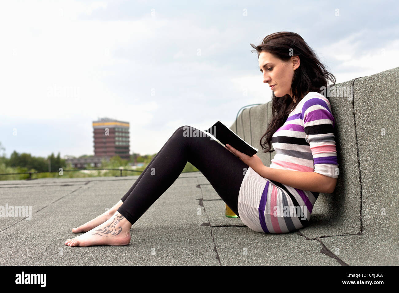 Deutschland, Hamburg, junge Frau sitzt auf dem Dach und Buch Stockfoto