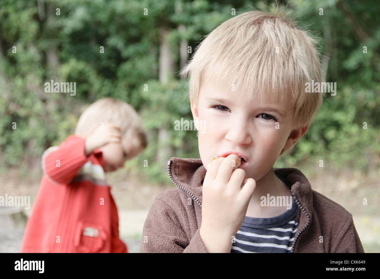 Junge, Essen im Freien während der jüngere Bruder spielt im Hintergrund (Indre et Loire, Frankreich). Stockfoto