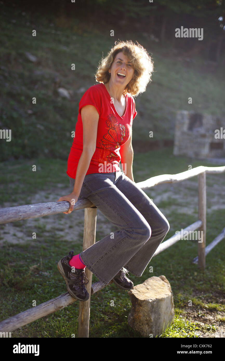 Glückliche mittlere gealterte Frau sitzt auf einem Zaun. Stockfoto