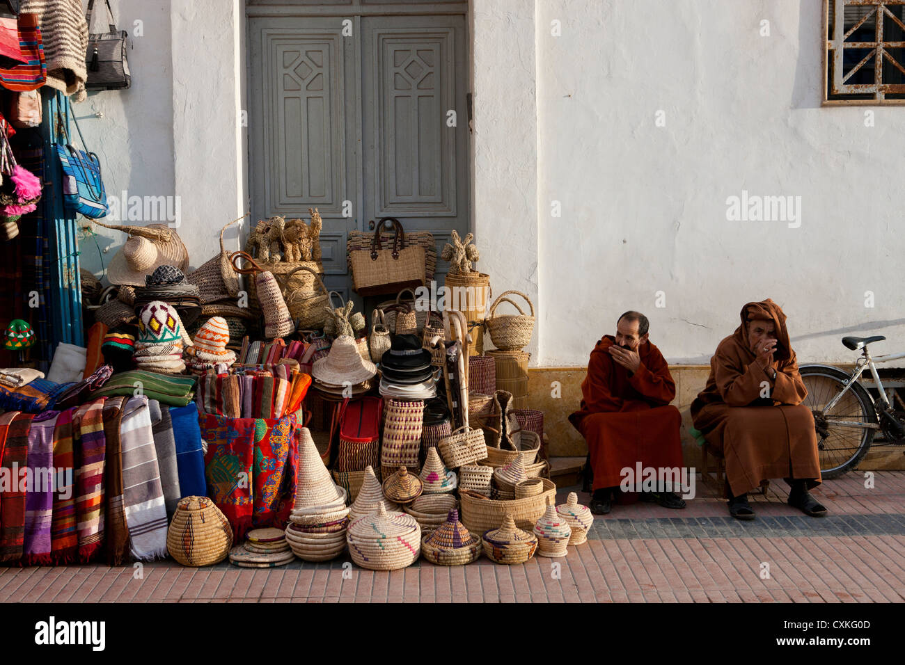 Zwei marokkanische Männer sitzen außerhalb von Shop mit Körbe, Tücher und Souvenirs in Essaouira, Marokko Stockfoto