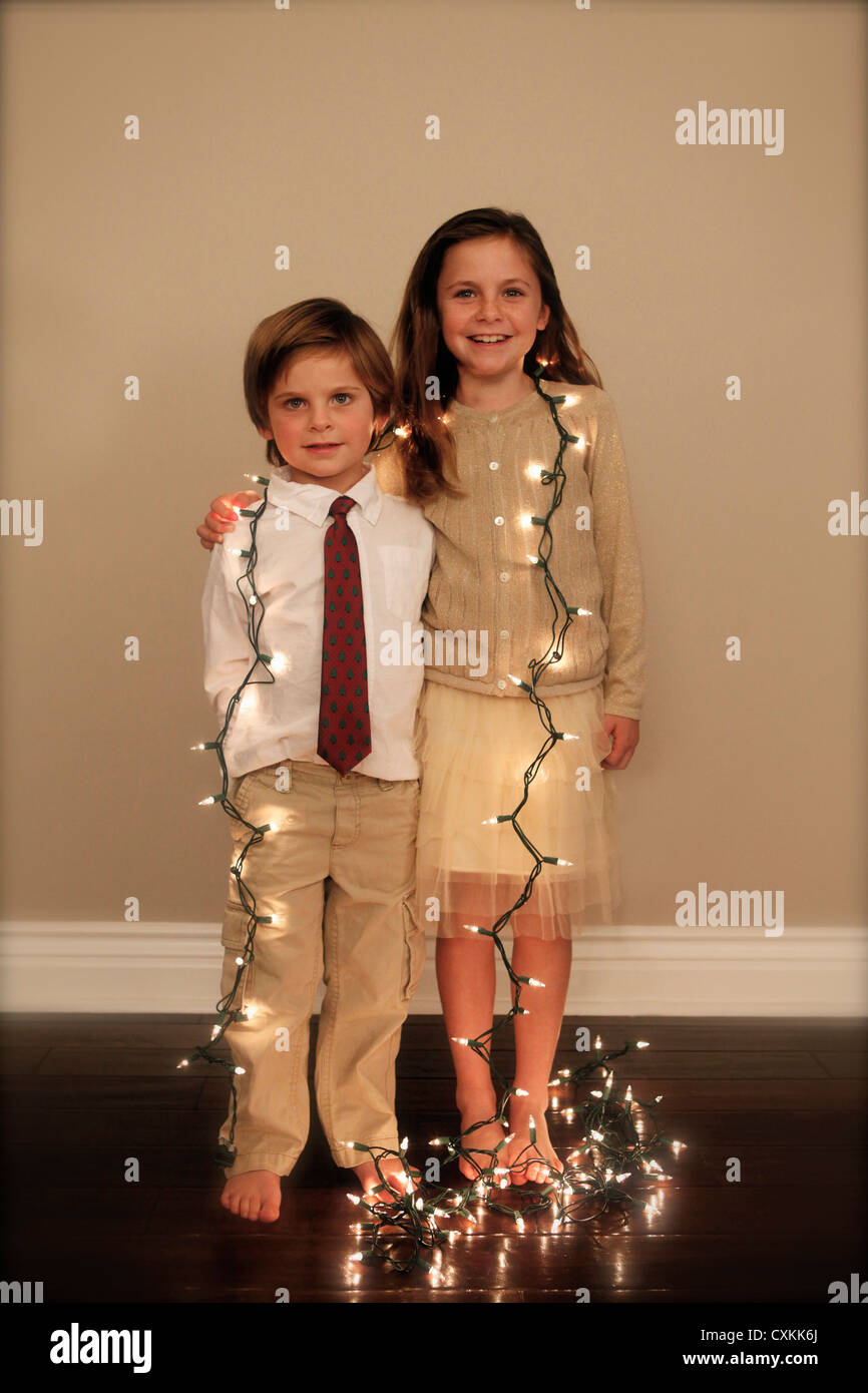 Bruder und Schwester gewickelt in Weihnachtsbeleuchtung Stockfoto