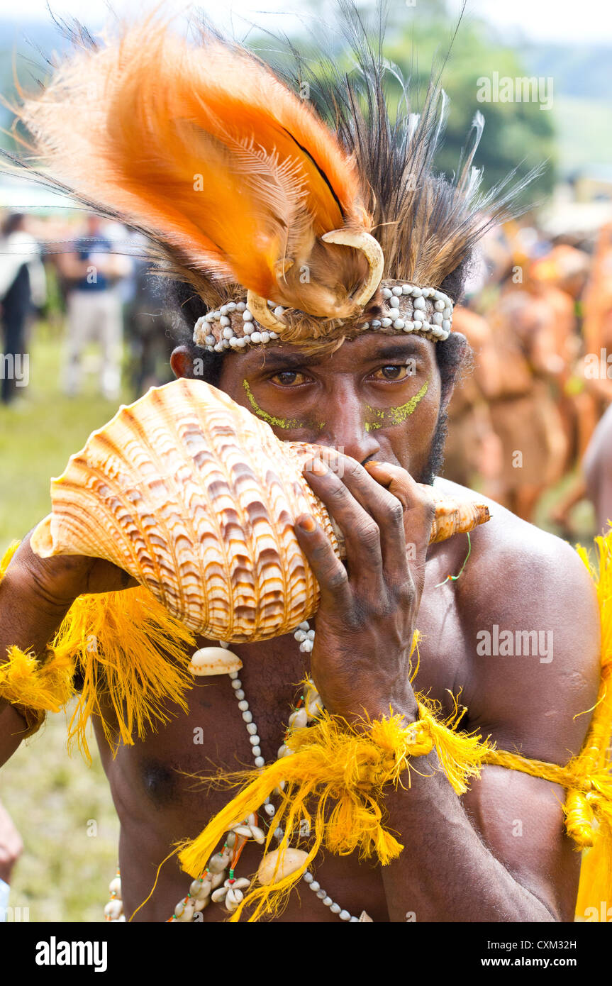 Mann trägt Tracht tribalen und bläst in eine Schale bei Singsing Goroka Festival, Papua New Guinea Stockfoto