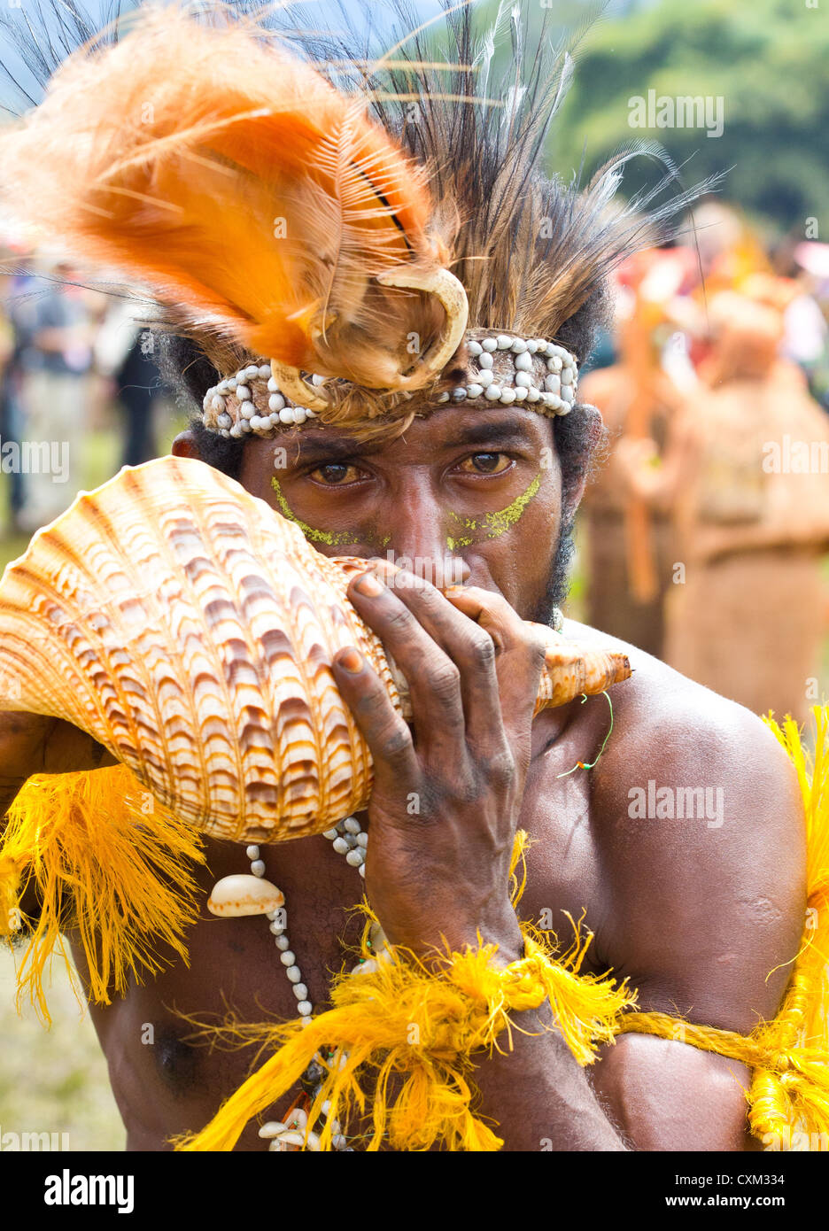 Mann trägt Tracht tribalen und bläst in eine Schale bei Singsing Goroka Festival, Papua New Guinea Stockfoto