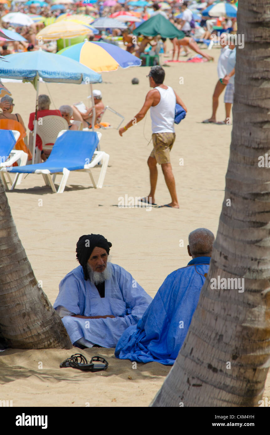 zwei arabische Menschen im Chat am Strand, während die Touristen die Sonne genießen Stockfoto