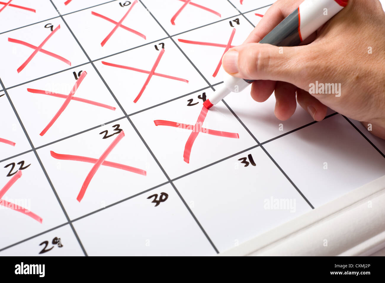 Eine Hand mit einem trockenen löschen Marker x'ing Tage des Monats aus einem Kalender. Laufe der Zeit Konzept. Stockfoto