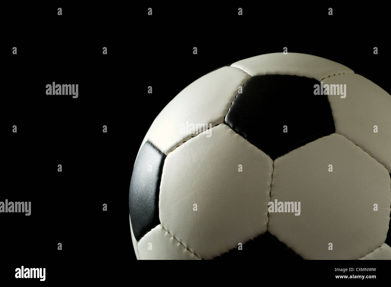 Fußball oder Fußball auf schwarzem Hintergrund beleuchtet, von der Seite - Raum auf der linken Seite für Kopie Stockfoto