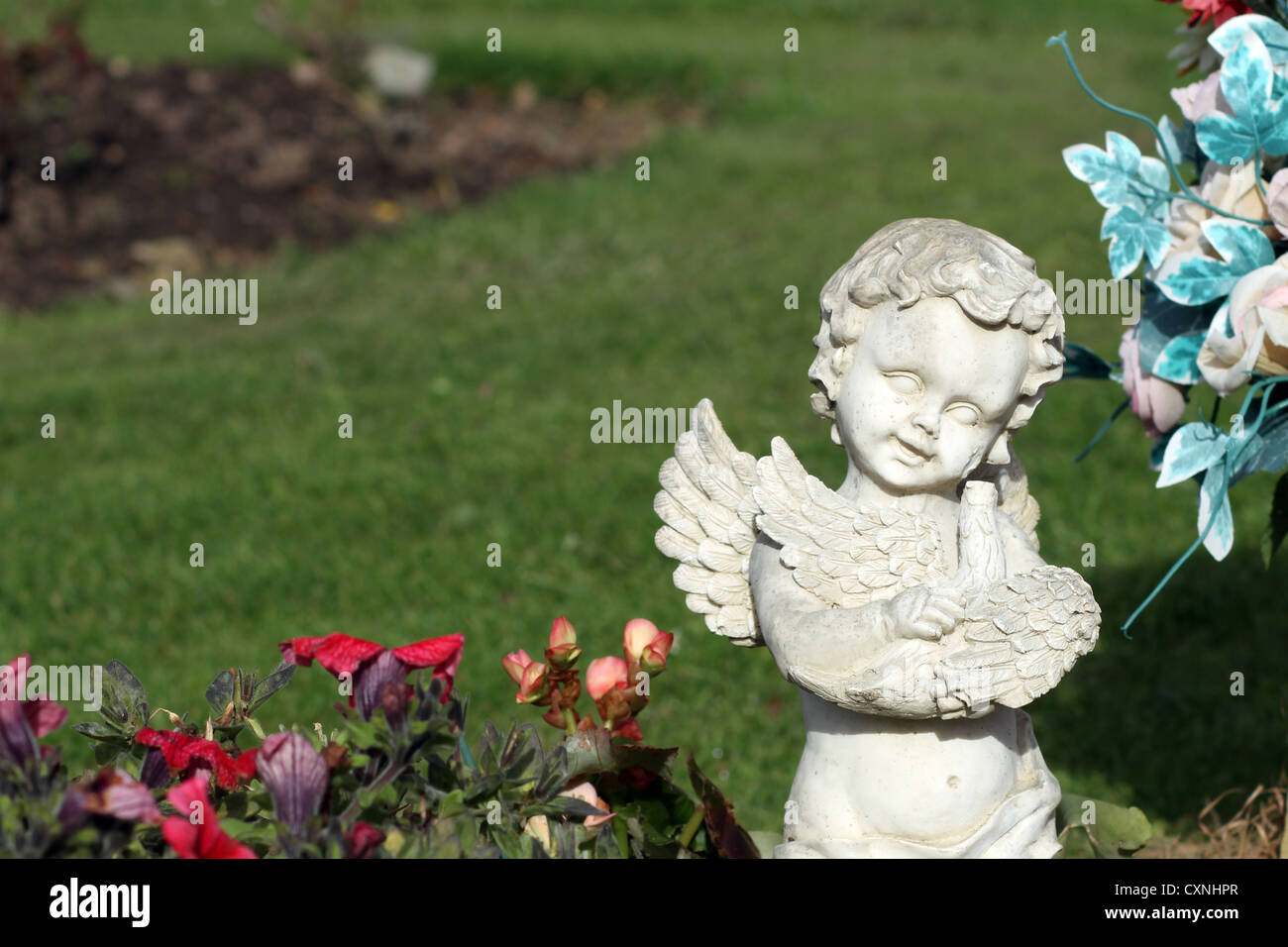 Engel-Denkmal im Friedhof neben blühenden Blumen. Stockfoto