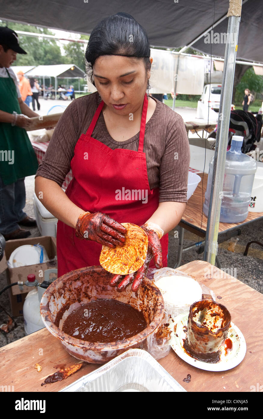 Hispanic Frau bereitet traditionelle mexikanische Enchiladas bedeckt Mais-Tortilla mit roten Chili Sauce auf Outdoor-Kirchtag Stockfoto