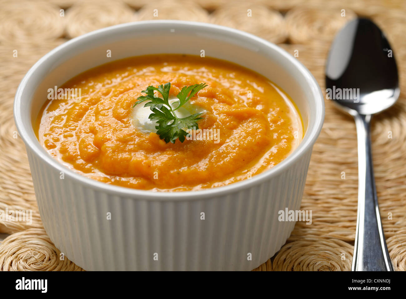 Karotten Suppe mit Sahne und Petersilie in weiße Schüssel für Gewebe aus Gras Tischset und Löffel Stockfoto