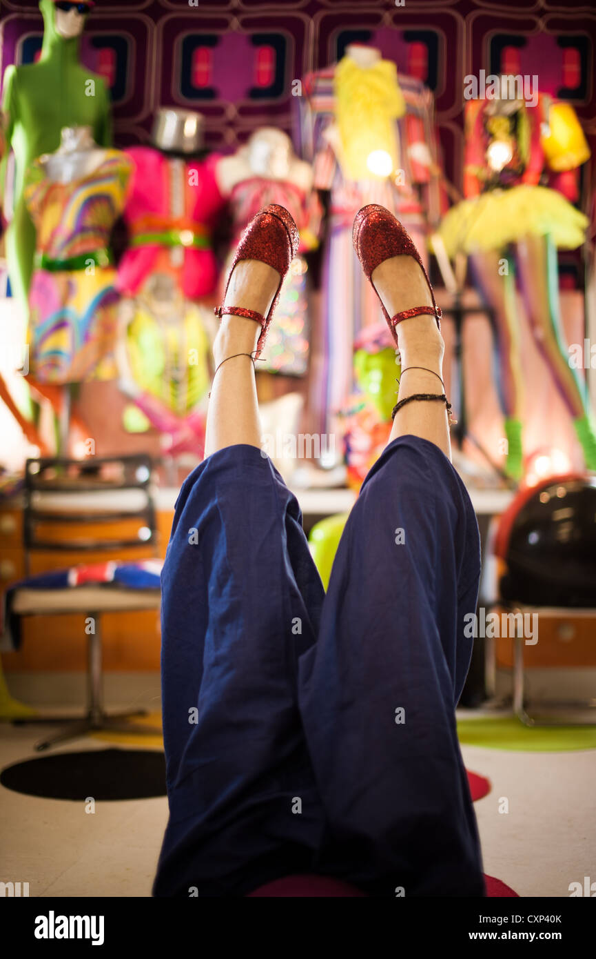 Eine Frau mit roten glitzernden Plateauschuhen im Ladengeschäft Brigtly gefärbt, ihre Füße in der Luft Stockfoto