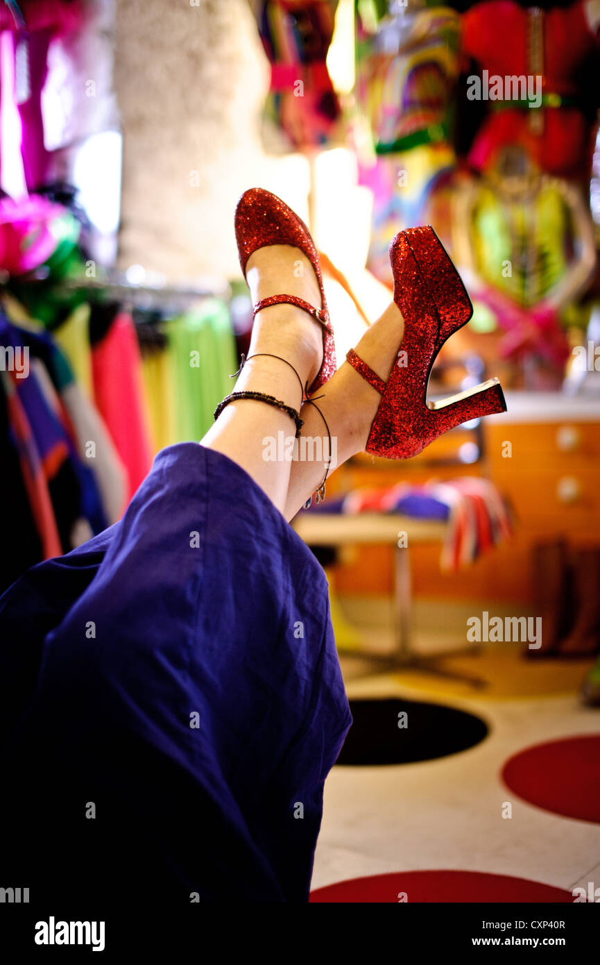 Eine Frau mit roten glitzernden Plateauschuhen im Ladengeschäft Brigtly gefärbt, ihre Füße in der Luft Stockfoto