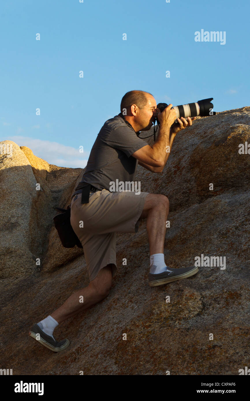 Fotograf mit Teleobjektiv stehend auf einem großen Felsen, Alabama Hills, Lone Pine, Kalifornien, Vereinigte Staaten von Amerika Stockfoto