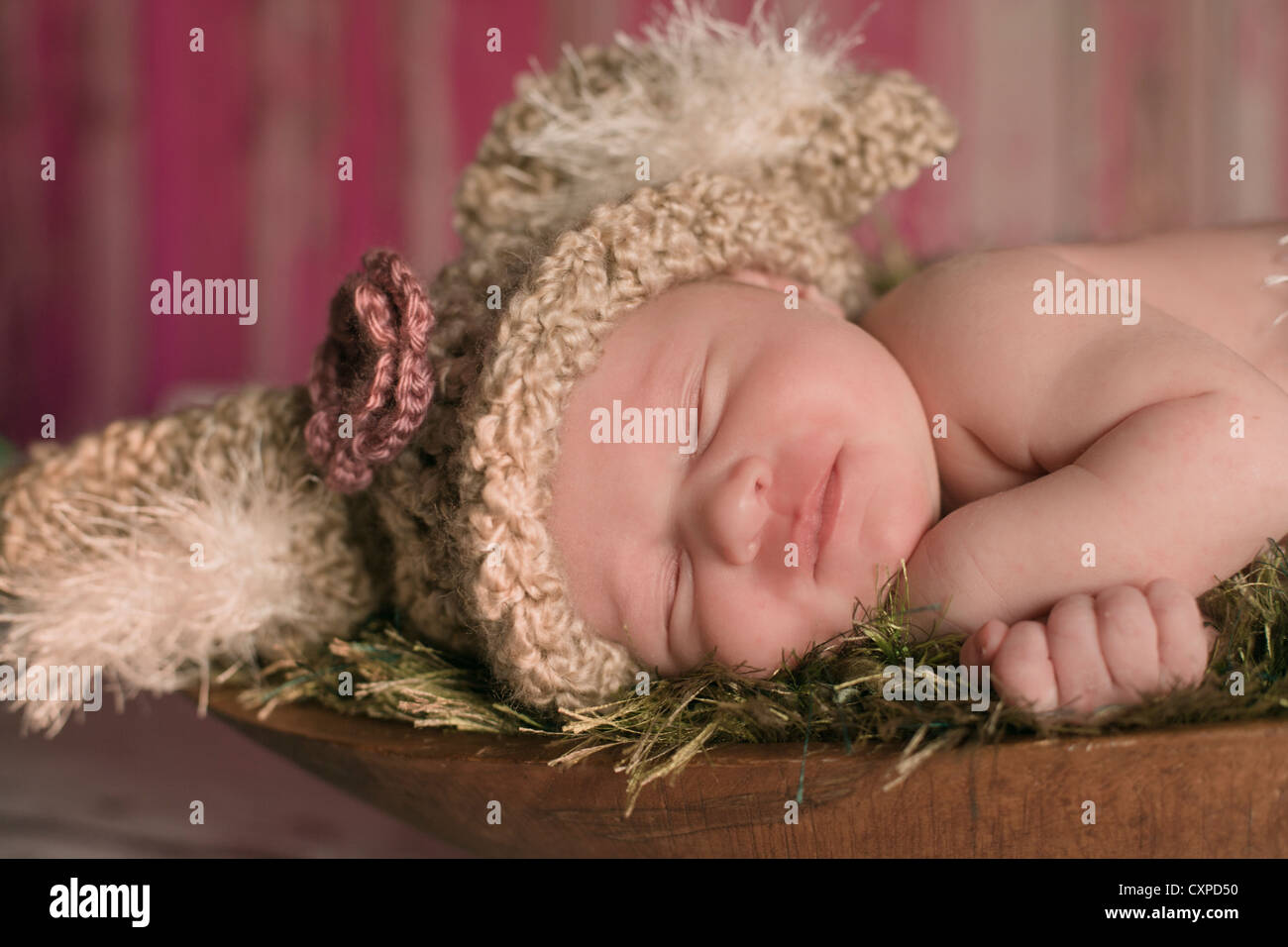 Neugeborenes Babymädchen gekleidet in Bunny Strickmütze schlafen in einer Holzschale. Stockfoto