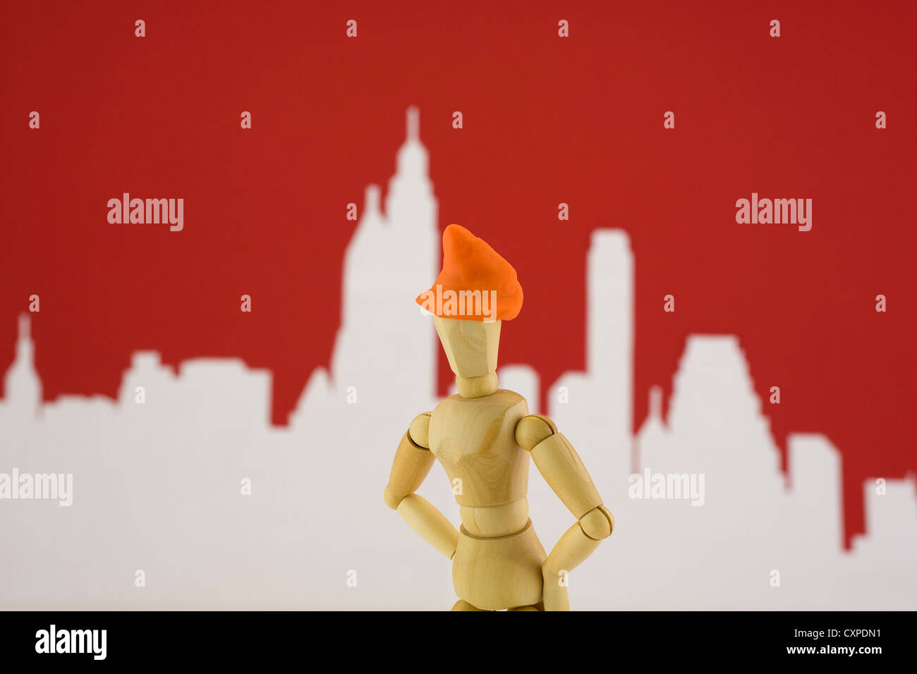 Stilvolle moderne orange Hut Puppe in einer neuen Stadt mit roten Skyline mit Gebäuden im Hintergrund. Stockfoto