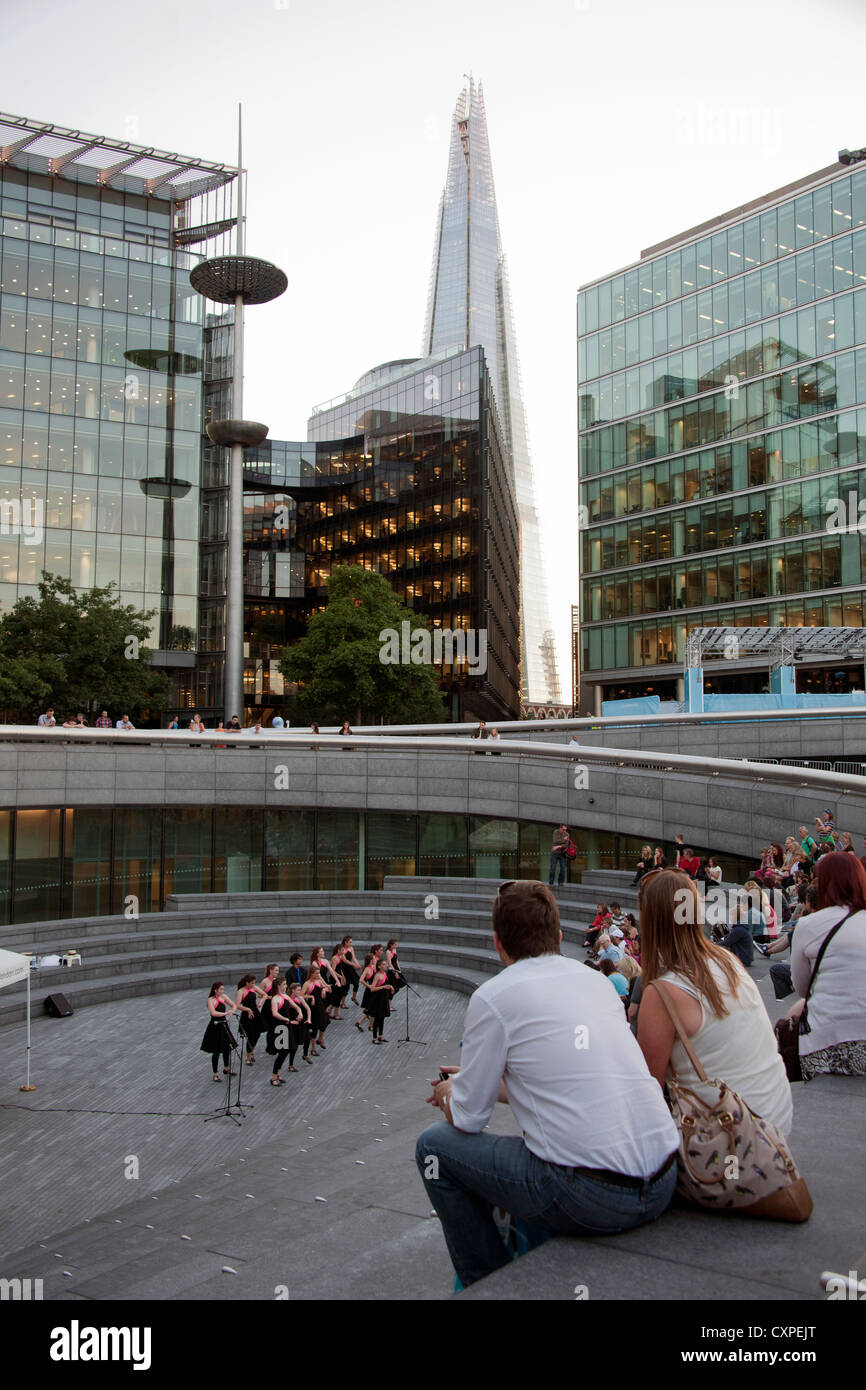 Leute zu beobachten eine Leistung auf die Schaufel, eine versunkene Amphitheater am More London mit der Scherbe im Hintergrund. Stockfoto