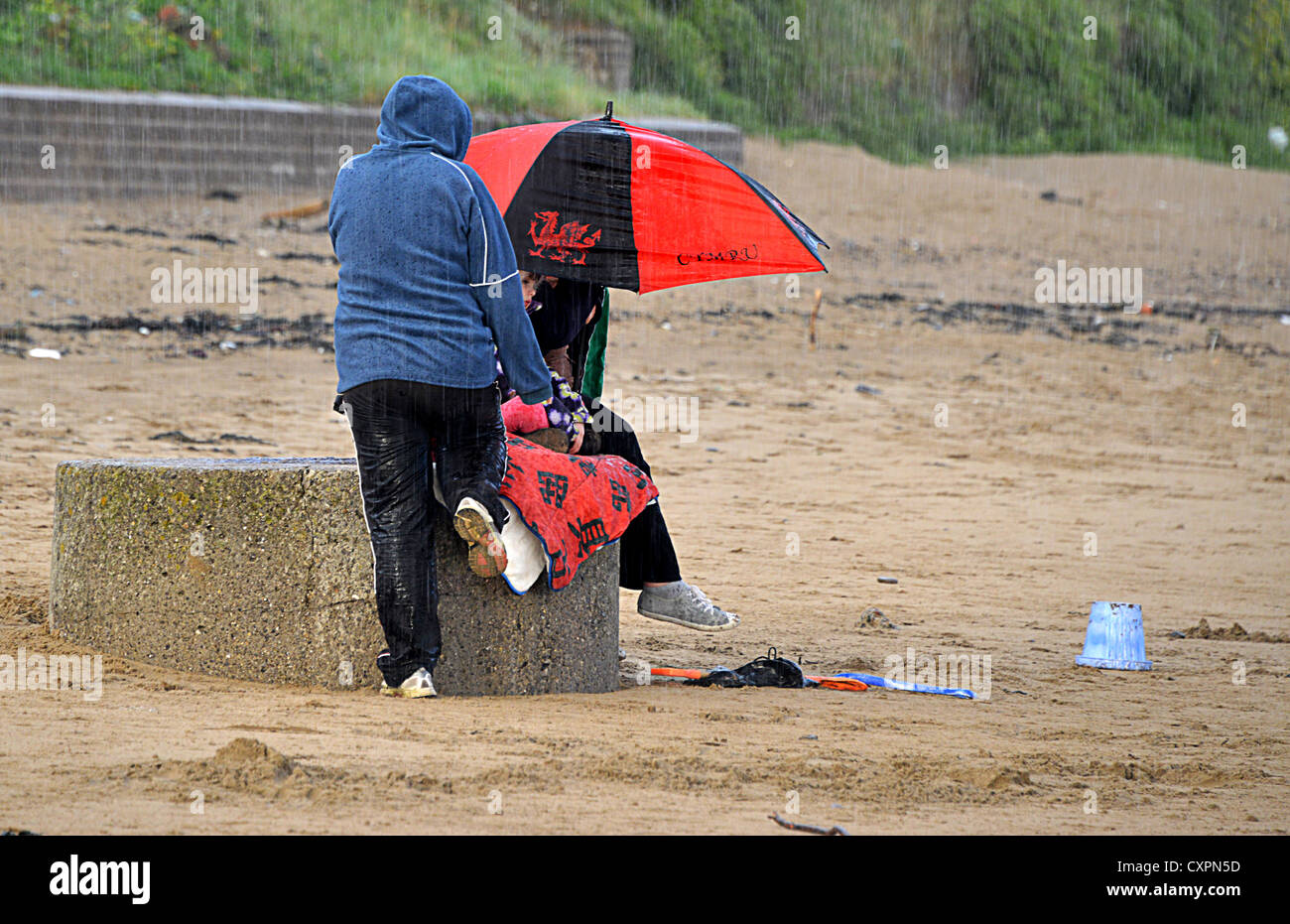 Junge Familie am Strand von Porthcawl gefangen in unerwarteten Platzregen Stockfoto