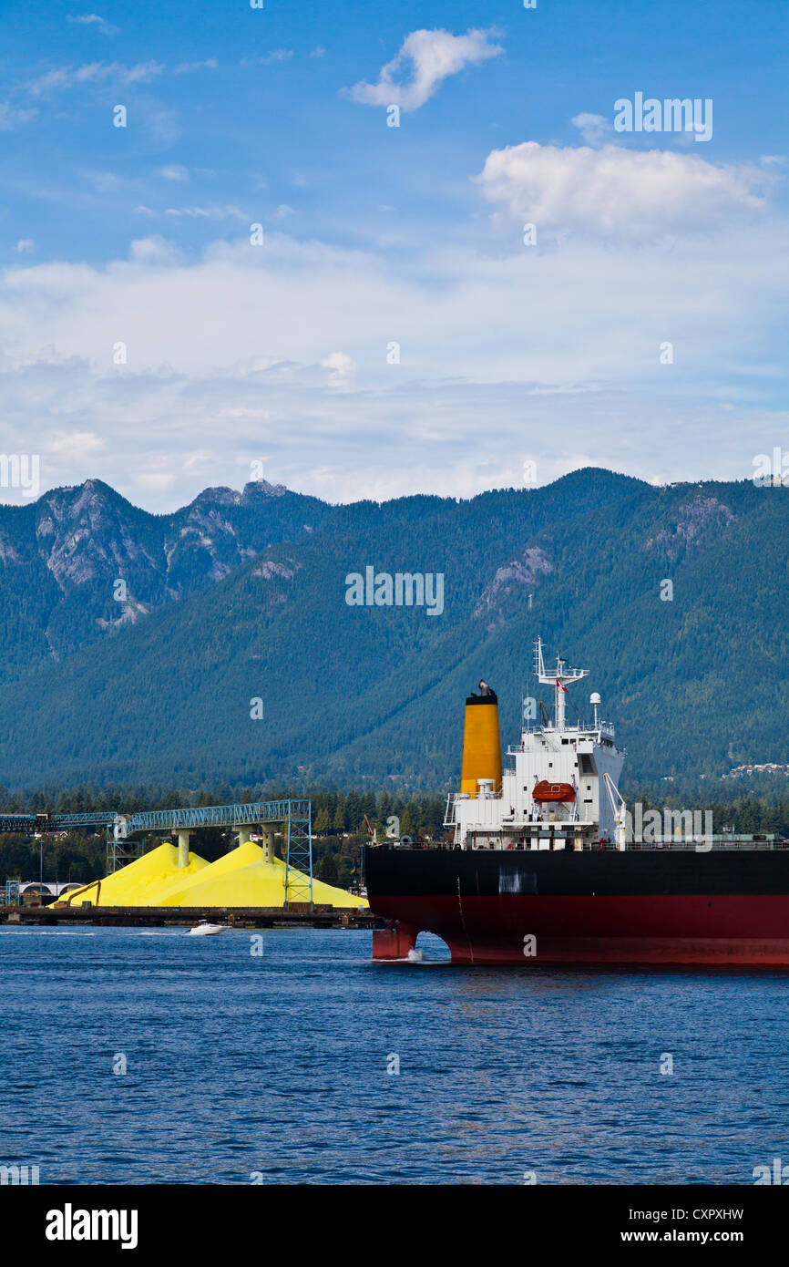 Ein Frachtschiff, Ankunft im Hafen von Vancouver, vorbei an Haufen von verarbeiteten gelben Schwefel. Stockfoto