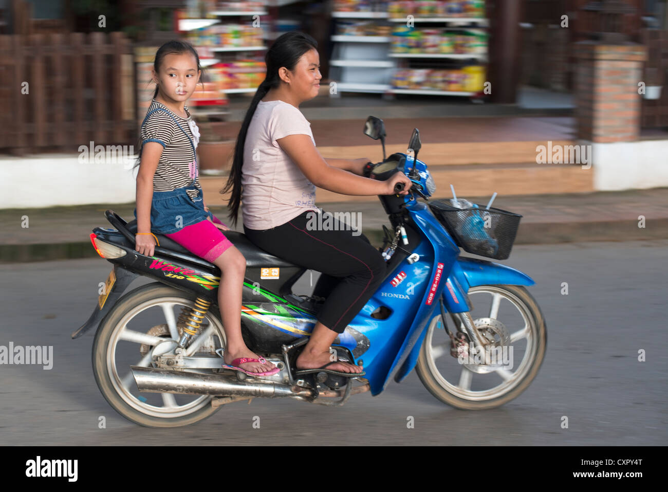 Eine Mädchen reitet Sozius auf ihre Mutter Motorrad in Luang Prabang, Laos. Stockfoto