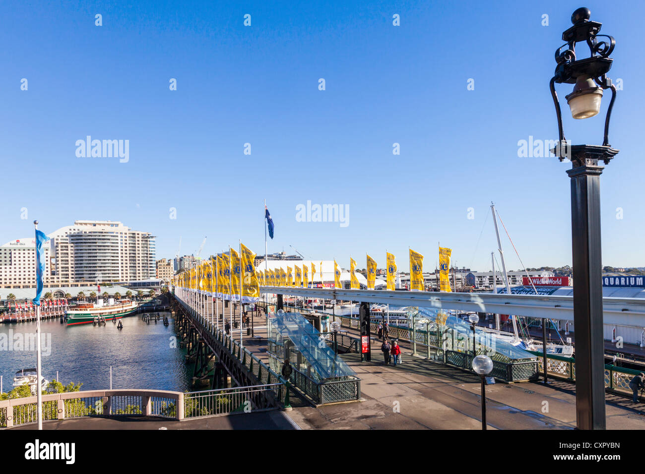 Die Pyrmont Bridge am Darling Harbour, dekoriert mit gelben Fahnen und die Aussicht über Cockle Bay, das Hotel Ibis. Stockfoto