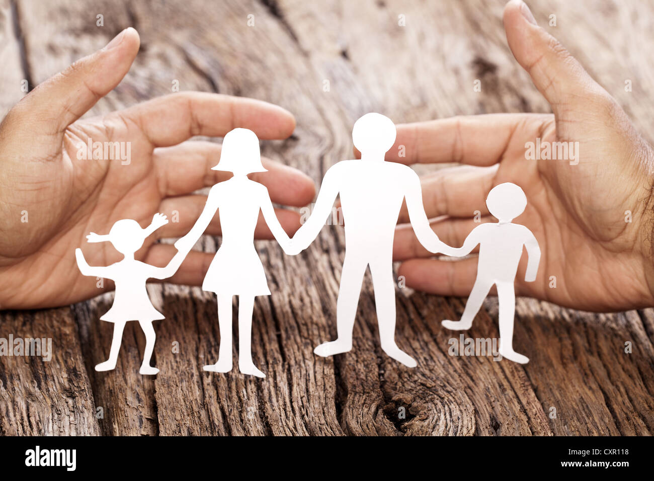 Pappfiguren der Familie auf einem Holztisch. Das Symbol der Einheit und des Glücks. Händen umarmen sanft die Familie. Stockfoto