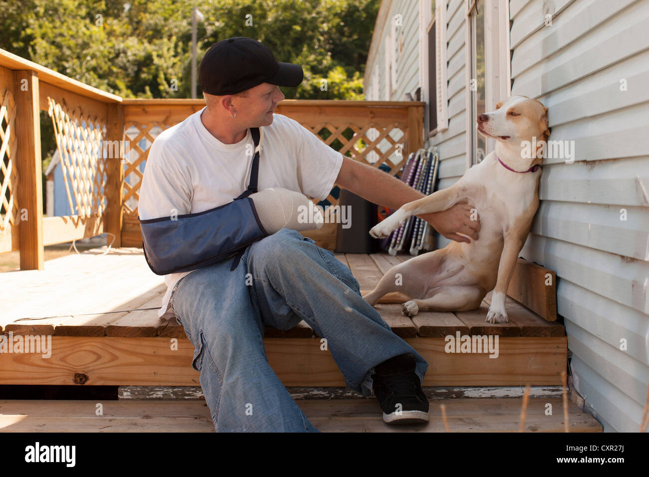 Mensch vor Haus mit Arm in der Schlinge und Hund Stockfoto