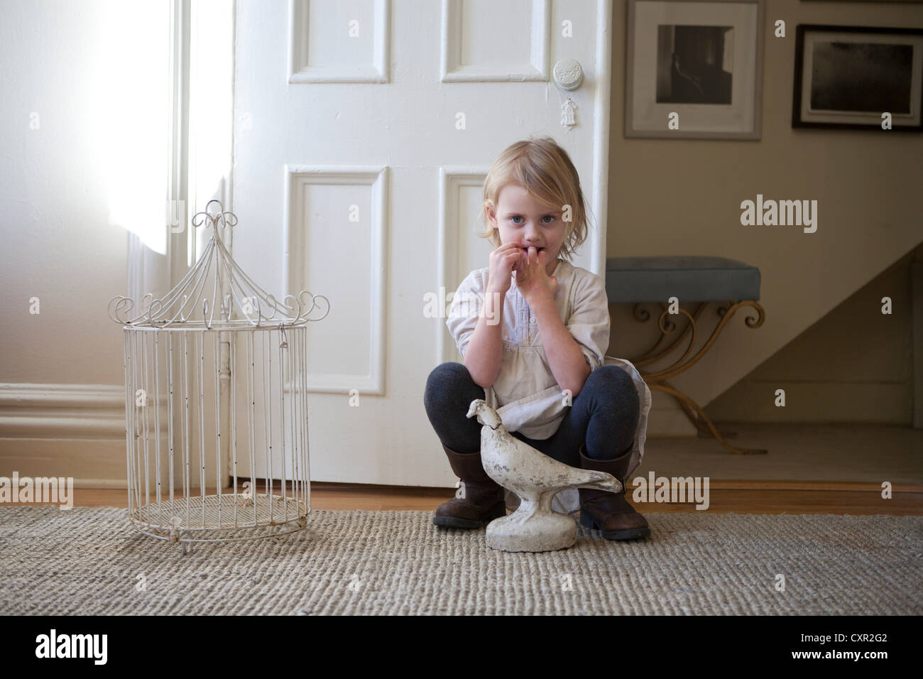 Kleines Mädchen durch die Tür mit Vogelkäfig und Vogel-statue Stockfoto