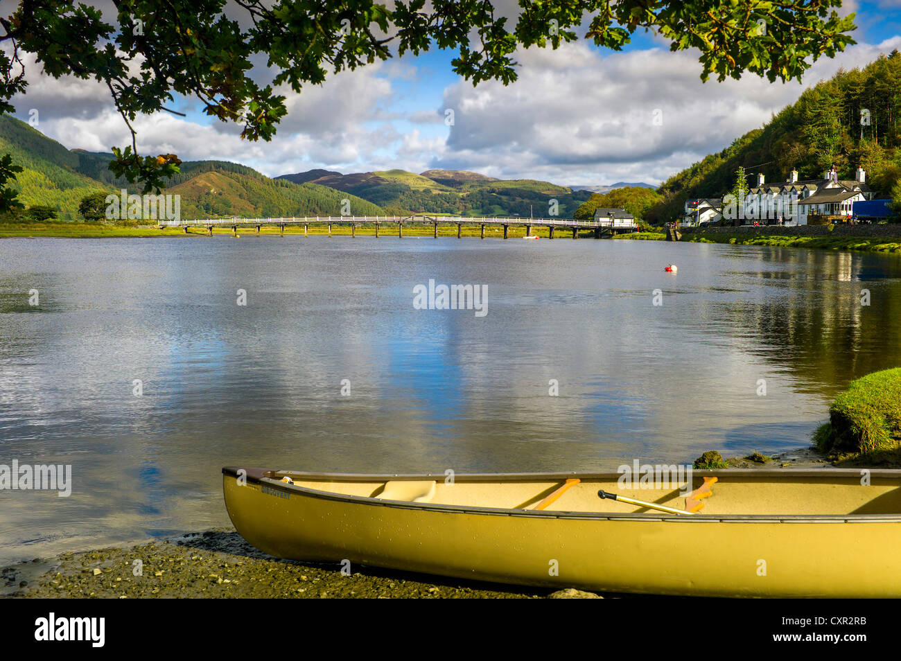 Ein gelbes Kanu im Vordergrund des Flusses Mawddach mit reflektierten blauen Himmel, Baum bedeckt Hügel, weiße Brücke im Hintergrund Stockfoto