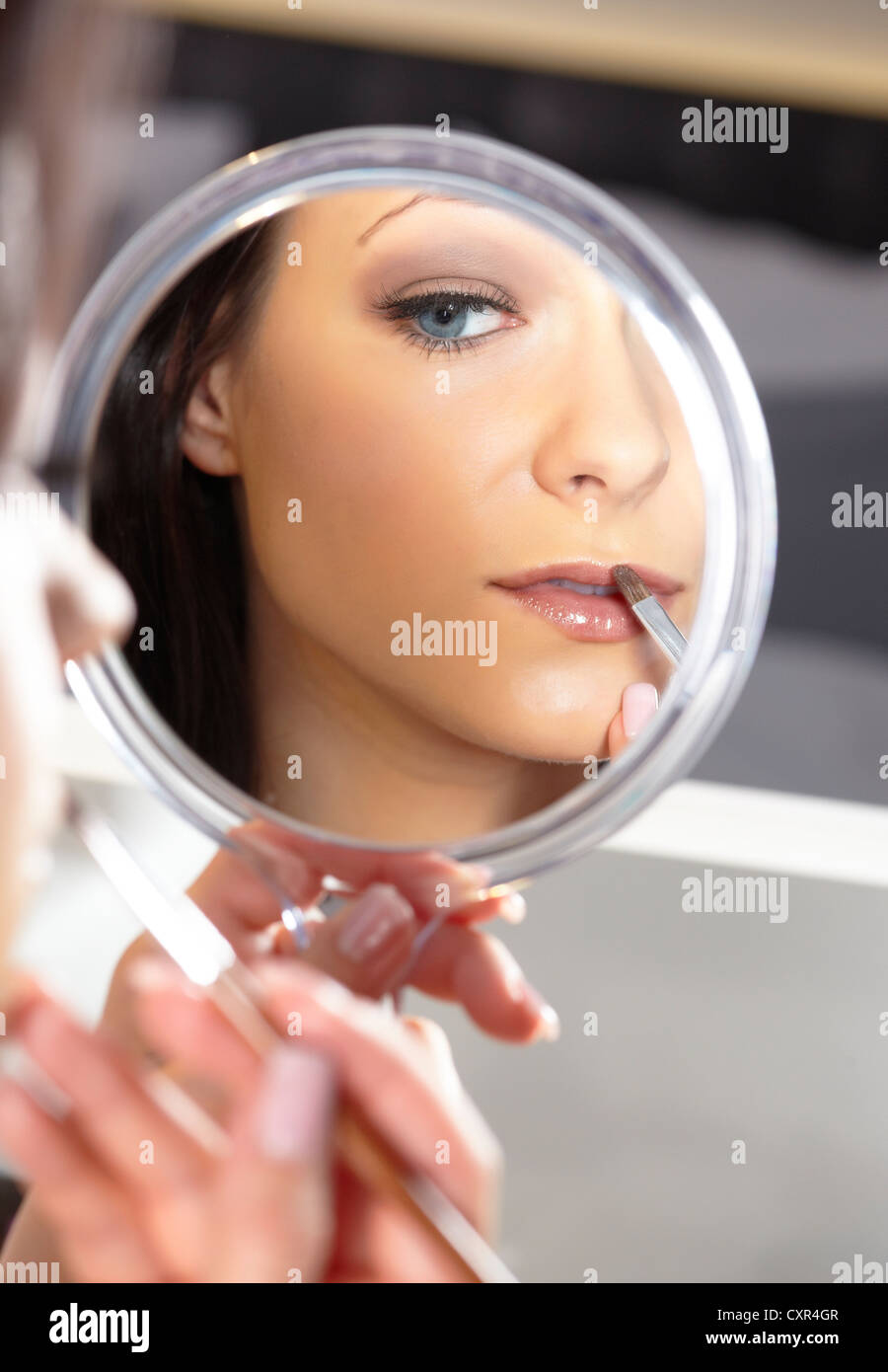 Junge Frau hält einen Handspiegel und einen Lippenstift-Pinsel Stockfoto
