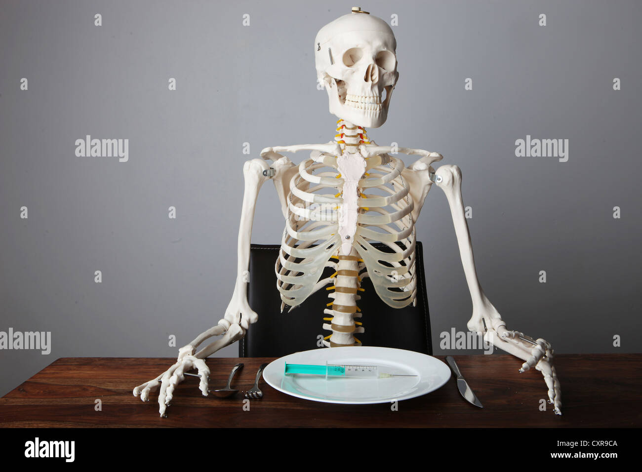 Skelett sitzen am gedeckten Tisch mit einer Spritze auf einem Teller Stockfoto