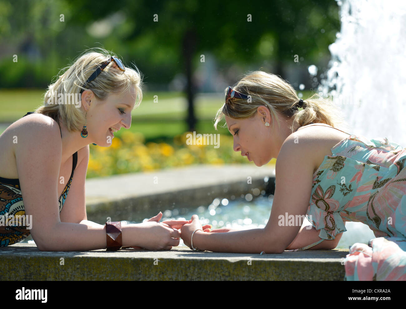 Zwei junge Frauen, Freunde, liegend auf einem Brunnen, Schlosspark Garten, Stuttgart, Baden-Württemberg, Deutschland, Europa, PublicGround Stockfoto