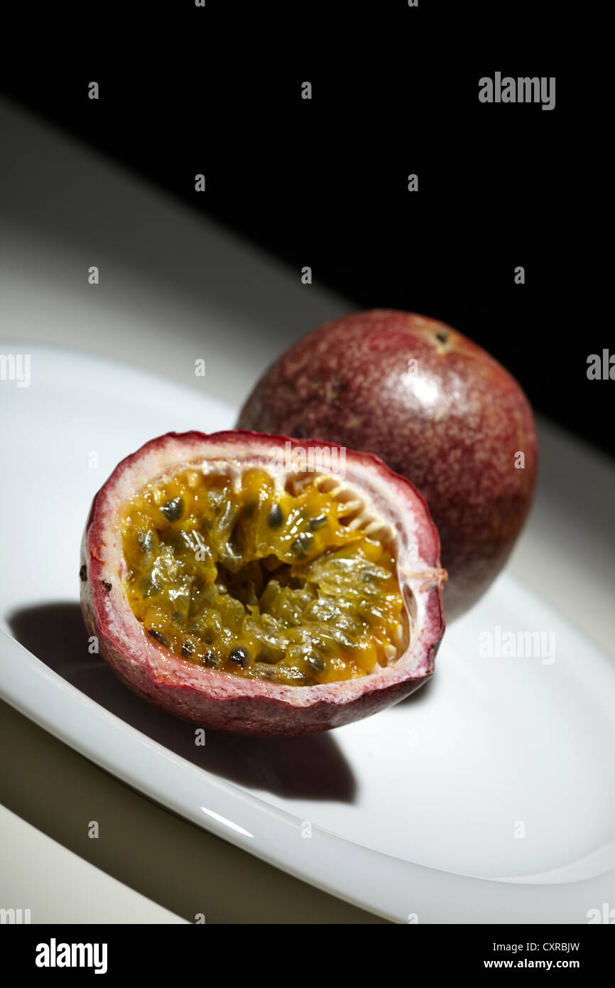 Passionsfrucht (Passiflora Edulis), einem ganzen und einer halbiert, auf einem weißen Teller Stockfoto