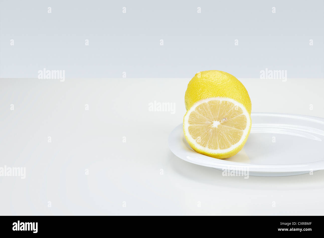 Zitrone (Citrus Limon), ganze und halbierte, auf einem weißen Teller Stockfoto