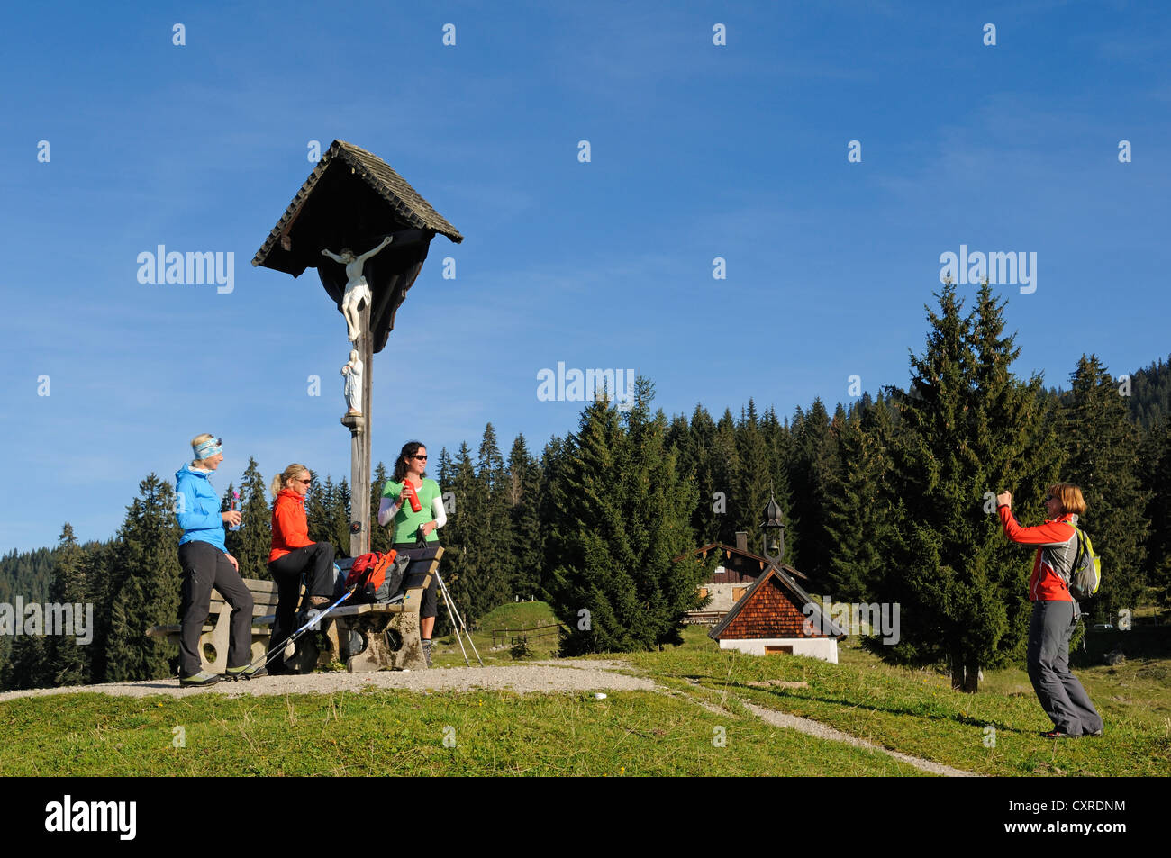 Weibliche Wanderer jemanden nehmen Sie ein Bild von ihnen vor ein Kreuz auf der Winklmoosalm Alm, Reit Im Winkl, Chiemgau, Bayern Stockfoto