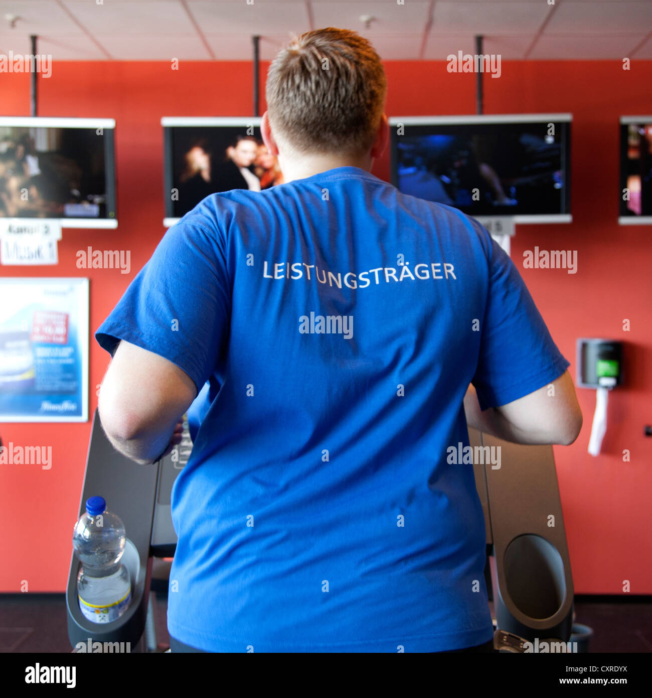 Sportler mit einem t-Shirt bekleidet, Schriftzug "Leistungstraeger", Deutsch für "Top Performer", laufen auf einem Laufband, Fitness-Center Stockfoto