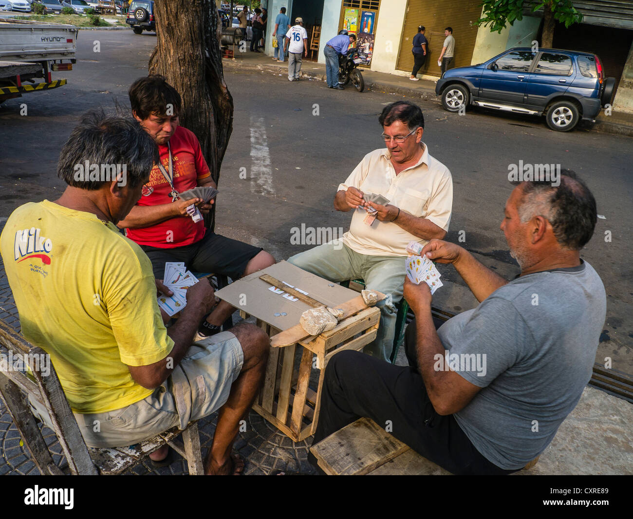 Vier ältere männliche Erwachsene spielen eine Partie Karten auf einem Bürgersteig in Asunción, Paraguay. Stockfoto