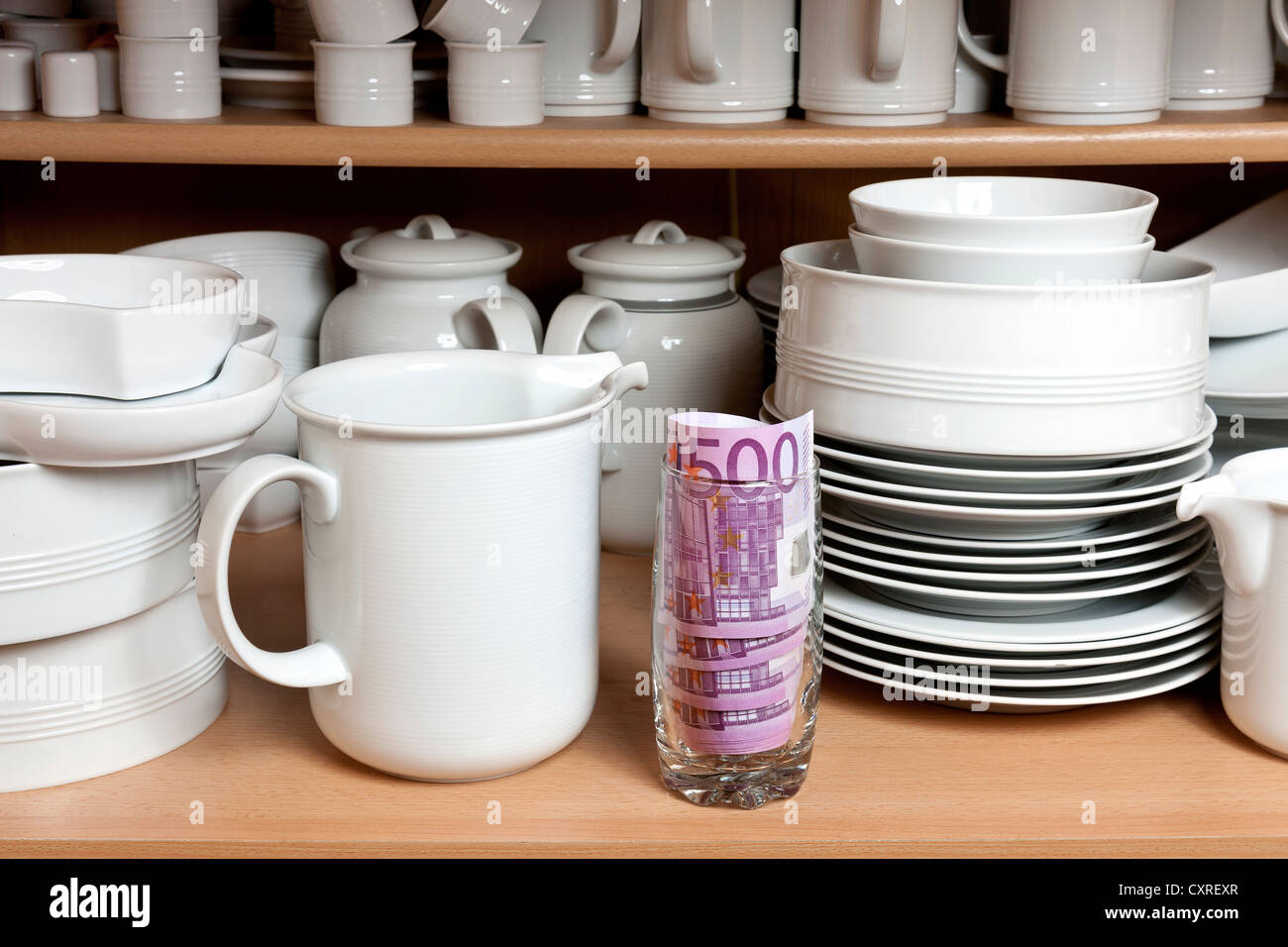 Geld im Küchenschrank, zwischen Tassen und Teller Stockfoto