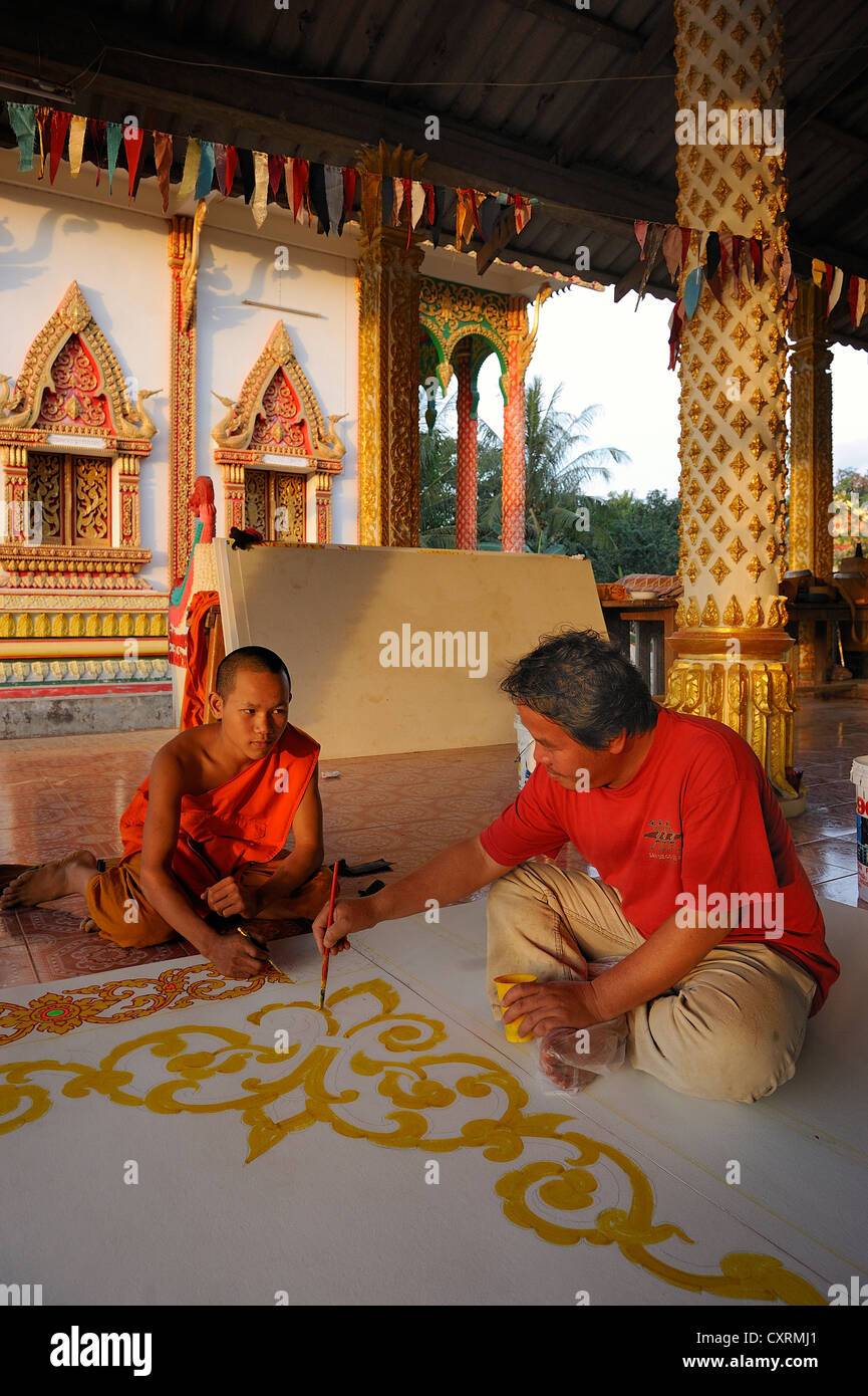 Ein Mönch und ein Handwerker Malerei Deckenplatten auf dem Boden von einem buddhistischen Tempel, Vang Vieng, Laos, Südostasien Stockfoto