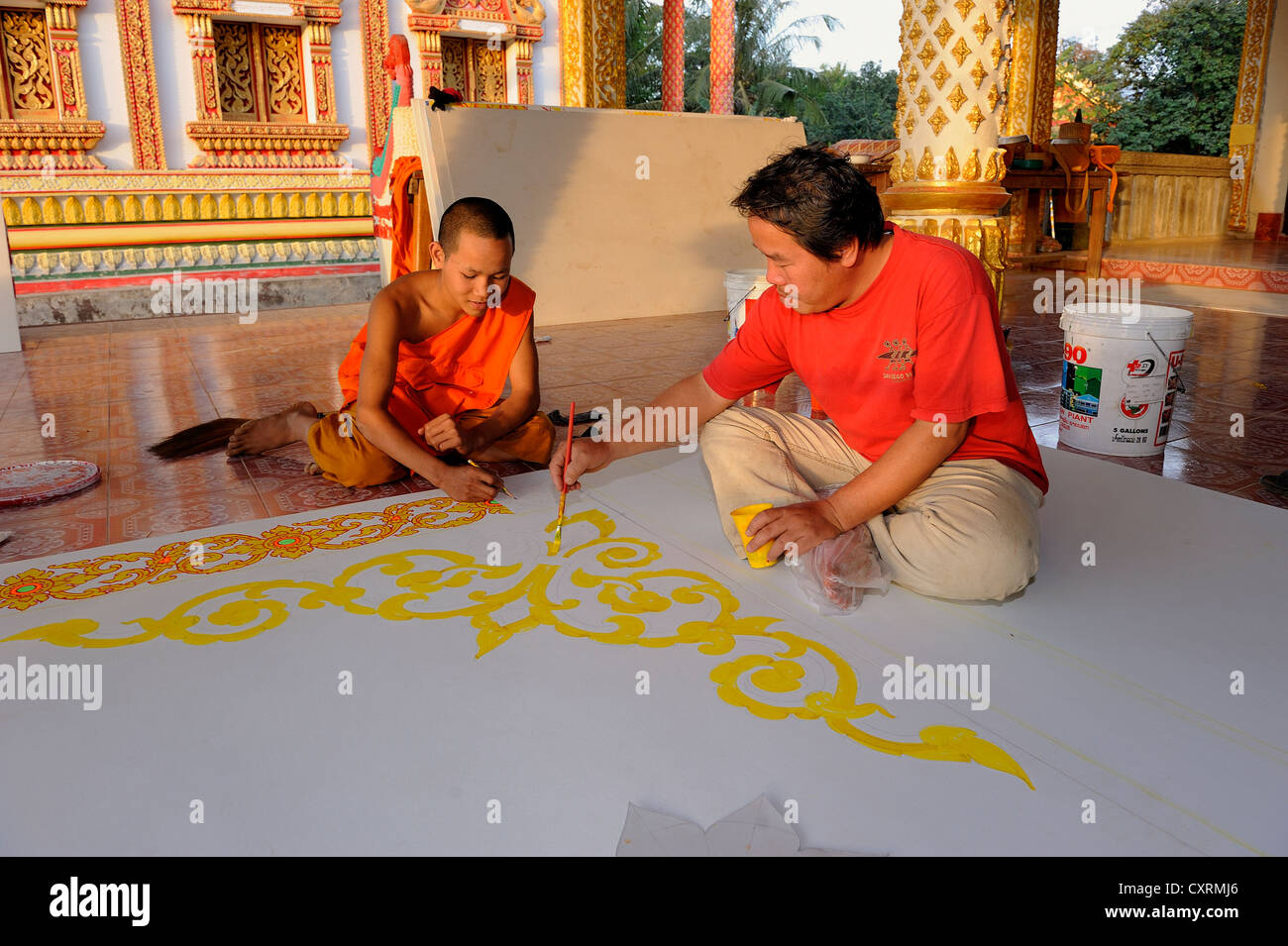 Ein Mönch und ein Handwerker Malerei Deckenplatten auf dem Boden von einem buddhistischen Tempel, Vang Vieng, Laos, Südostasien Stockfoto