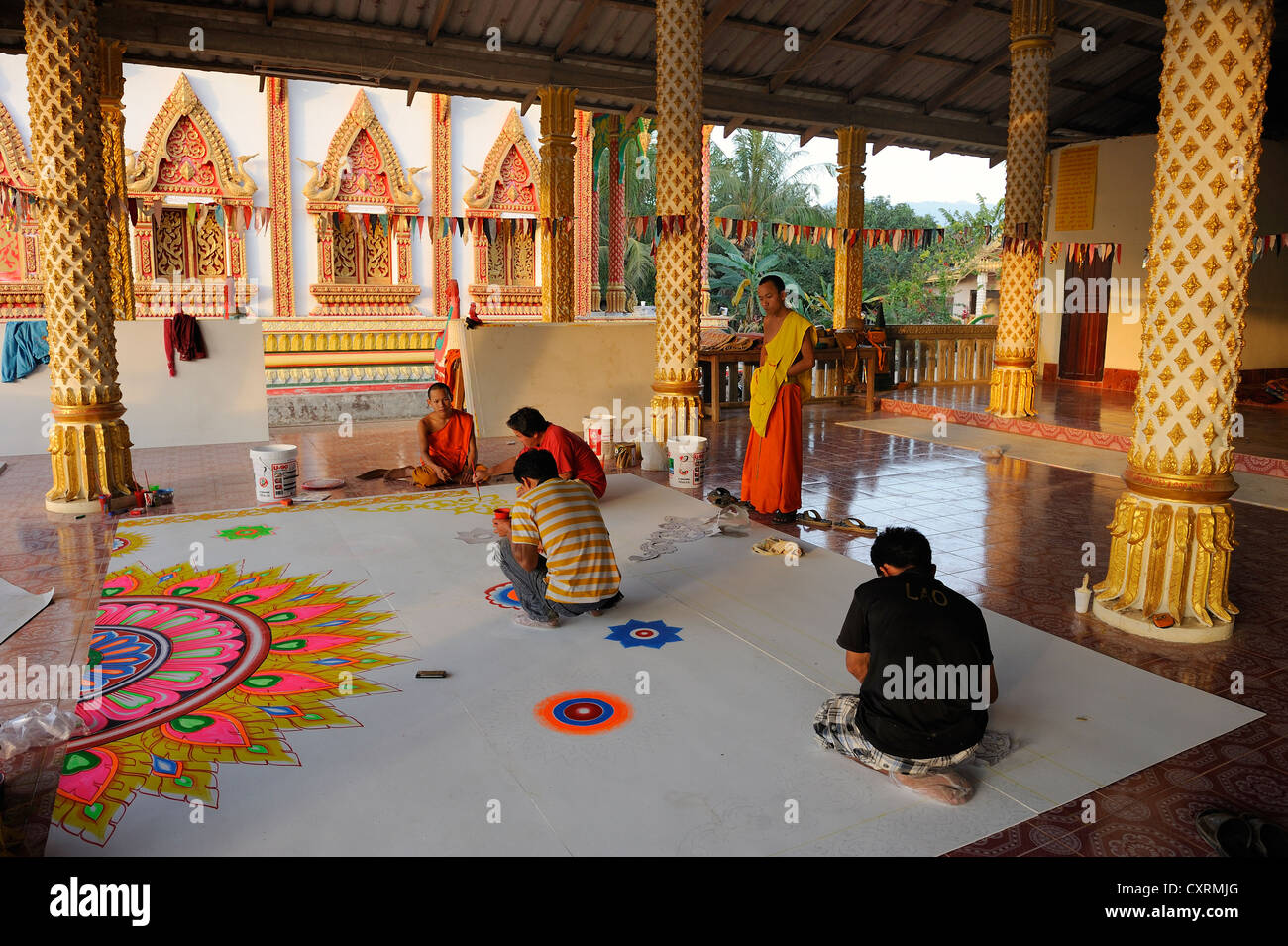 Ein Mönch und Handwerker Malerei Deckenplatten auf dem Boden von einem buddhistischen Tempel, Vang Vieng, Laos, Südostasien Stockfoto