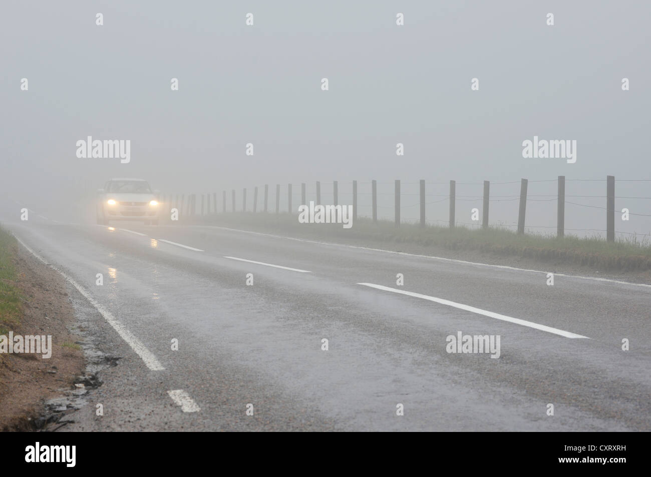 Auto mit Scheinwerfern unterwegs im dichten Nebel auf einer Straße in den schottischen Highlands, Grampian Mountains, Schottland, Vereinigtes Königreich Stockfoto