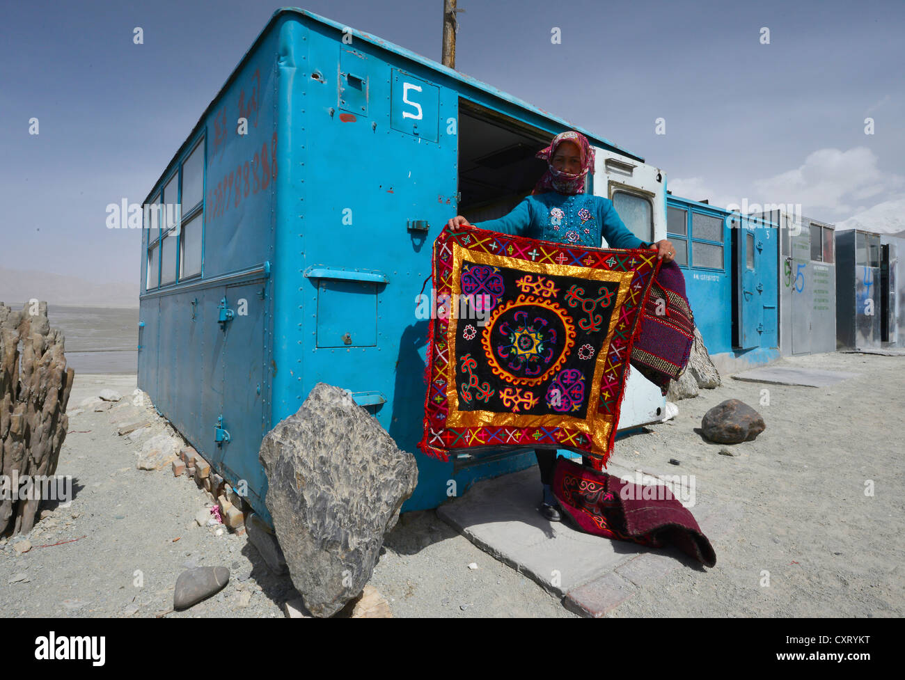Kasachische Frau zeigt eine Hand-Woven, gestickte Wand Teppich, einfache blaue Container, Haus-Boxen, Lagerbehälter, Geschäfte Stockfoto