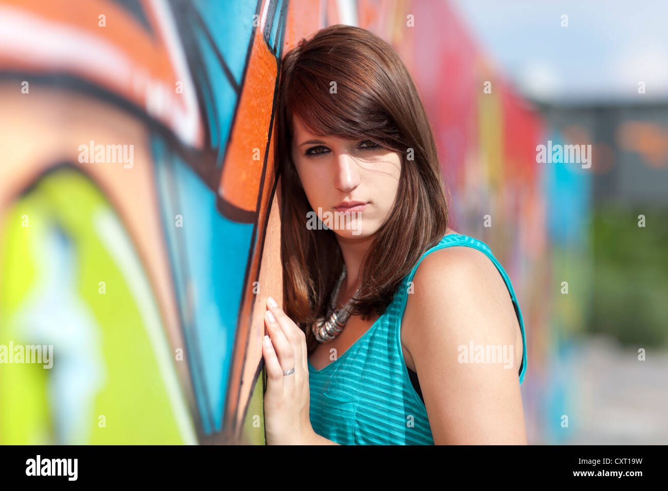 Junge Frau trägt ein türkises Top, schwarze Leggings und high Heels vor Wand mit Graffiti, Porträt Stockfoto