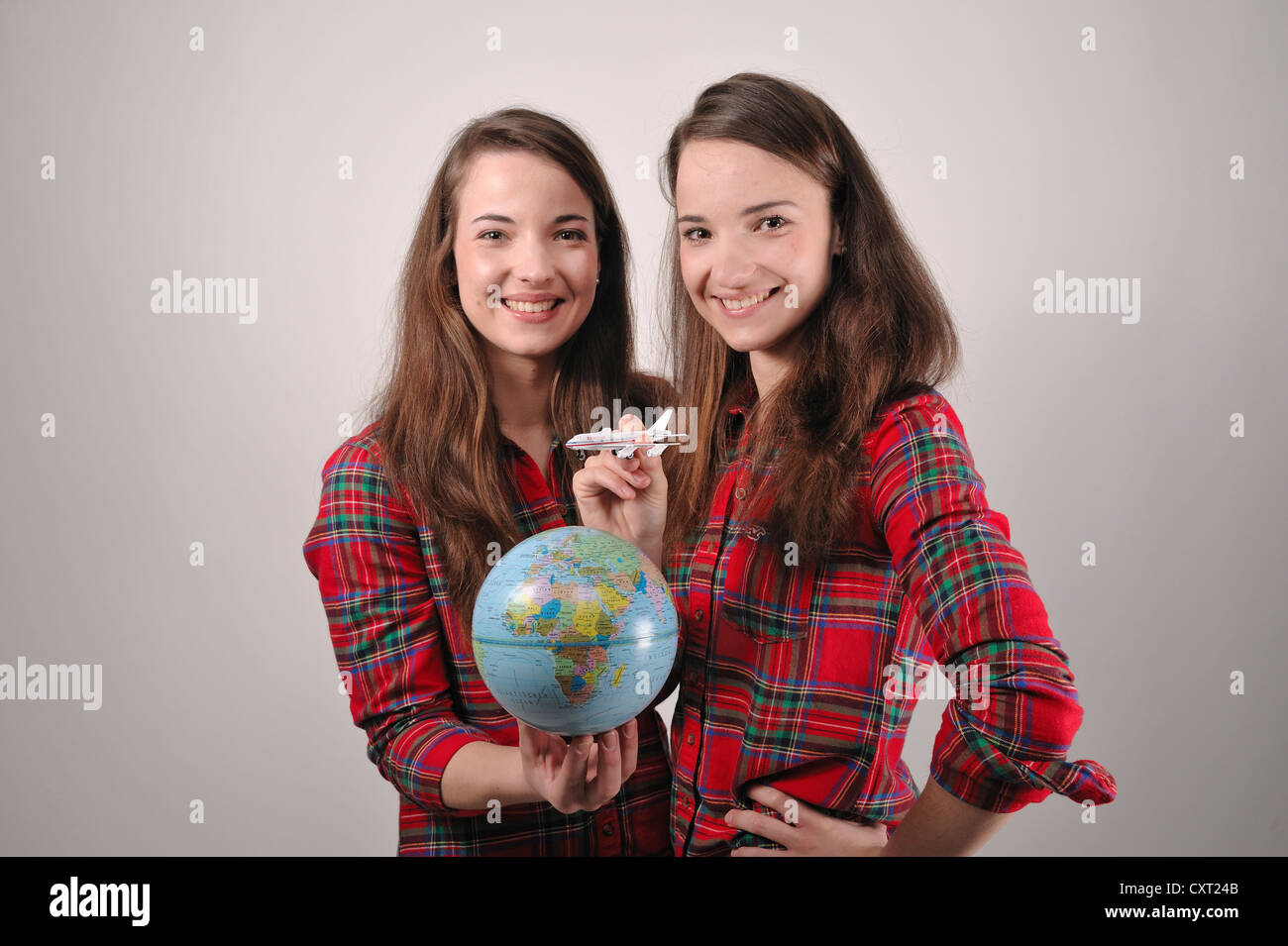 Zwillingsschwestern spielen eine Tour auf der ganzen Welt, ein Betrieb eine kleine Kugel, hält die andere ein Spielzeugflugzeug Stockfoto