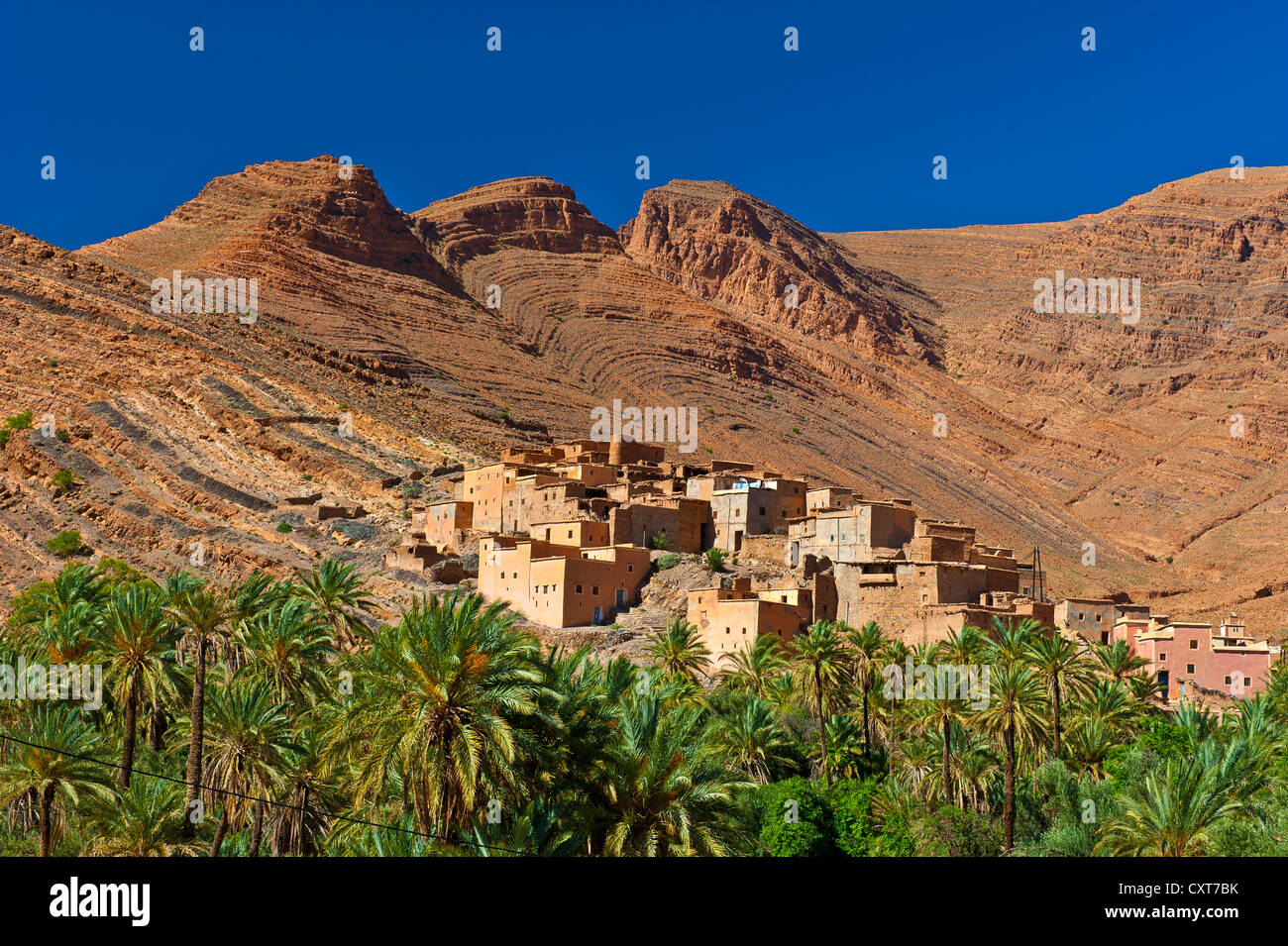 Kleiner Ton-Dorf und Dattelpalmen (Phoenix SP.) vor dem roten Berglandschaft im Tal Ait Mansour Stockfoto