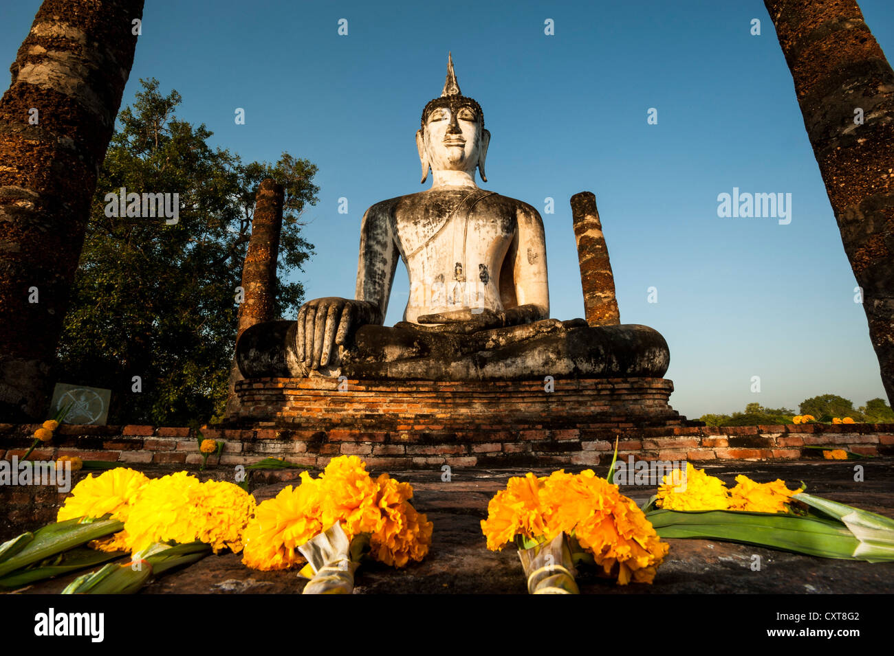 Blumen vor der sitzende Buddha-Statue im Wat Mahathat Tempel, Sukhothai Historical Park, UNESCO-Weltkulturerbe Stockfoto