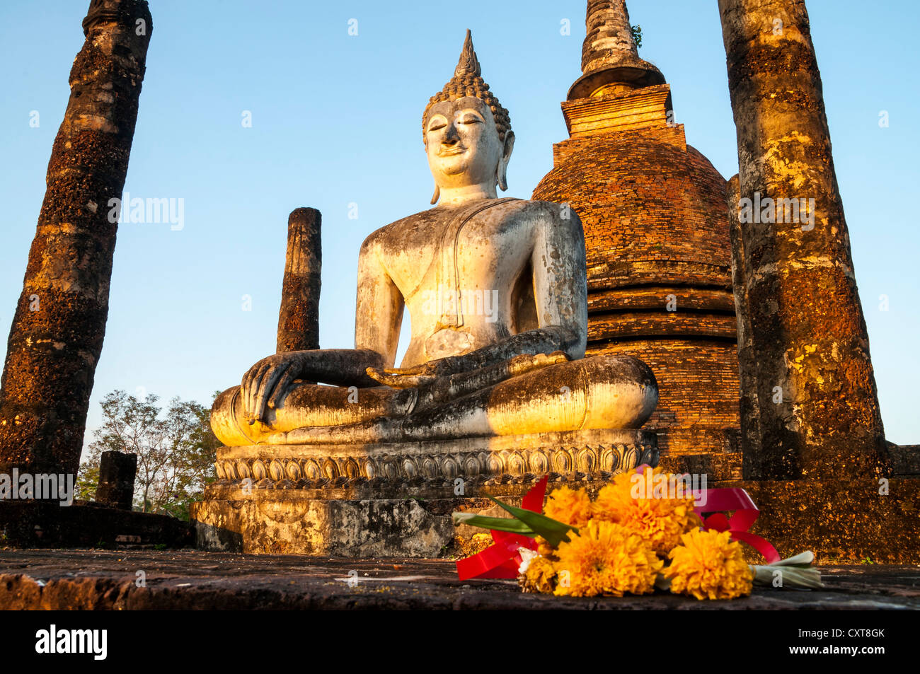 Blumen vor der sitzende Buddha-Statue im Wat Sa Si oder Sra Sri Tempel, Sukhothai Historical Park Stockfoto