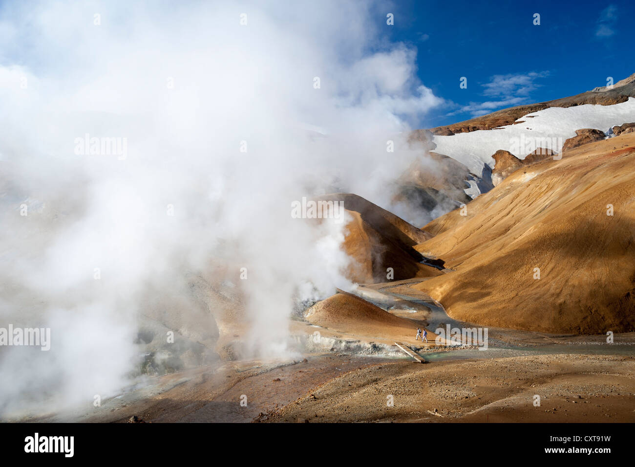 Wanderer auf einem Pfad, Brücke über einem dampfenden Bach, heiße Quellen und die schneebedeckten Berge der Rhyolith Stockfoto