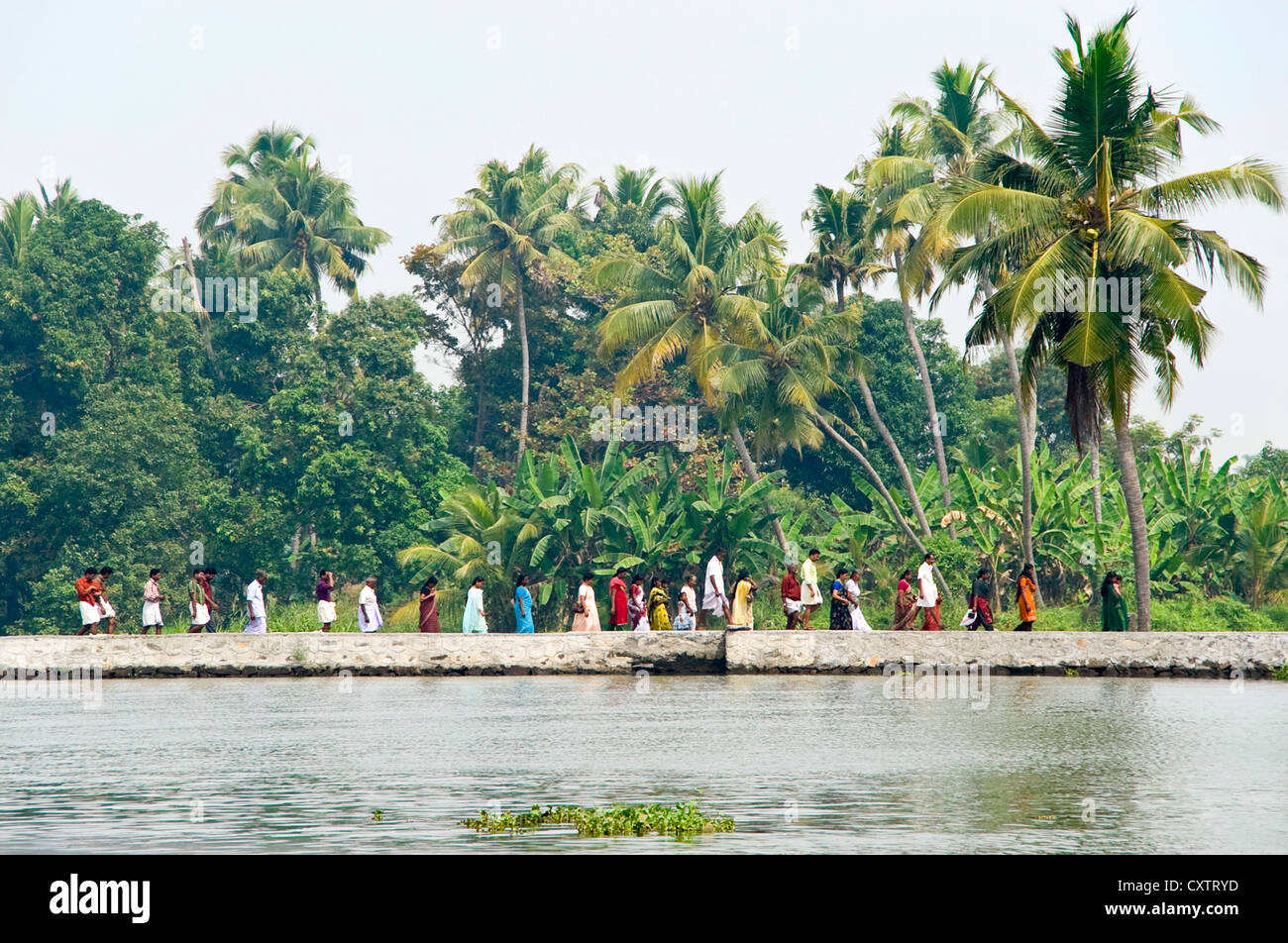 Horizontale Ansicht einer Linie des indischen Volkes zu Fuß entlang des Flussufers in Kerala. Stockfoto