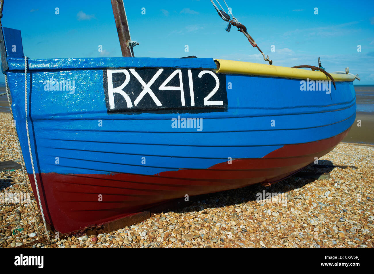 Helles Blau und rot Fischerboot hochgezogen auf einem Kiesstrand New Romney Kent UK Stockfoto